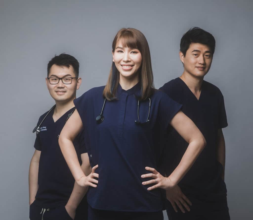 Three healthcare professionals, two men and one woman, in dark scrubs stand side by side, smiling confidently at the camera with stethoscopes around their necks, embodying the feeling of home care and dedication to their patients.