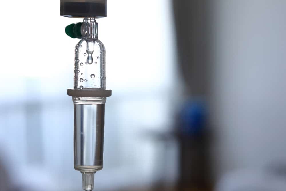 Close-up of an intravenous drip chamber with clear liquid inside, highlighting the precision and care involved in medical services, against a blurred background.