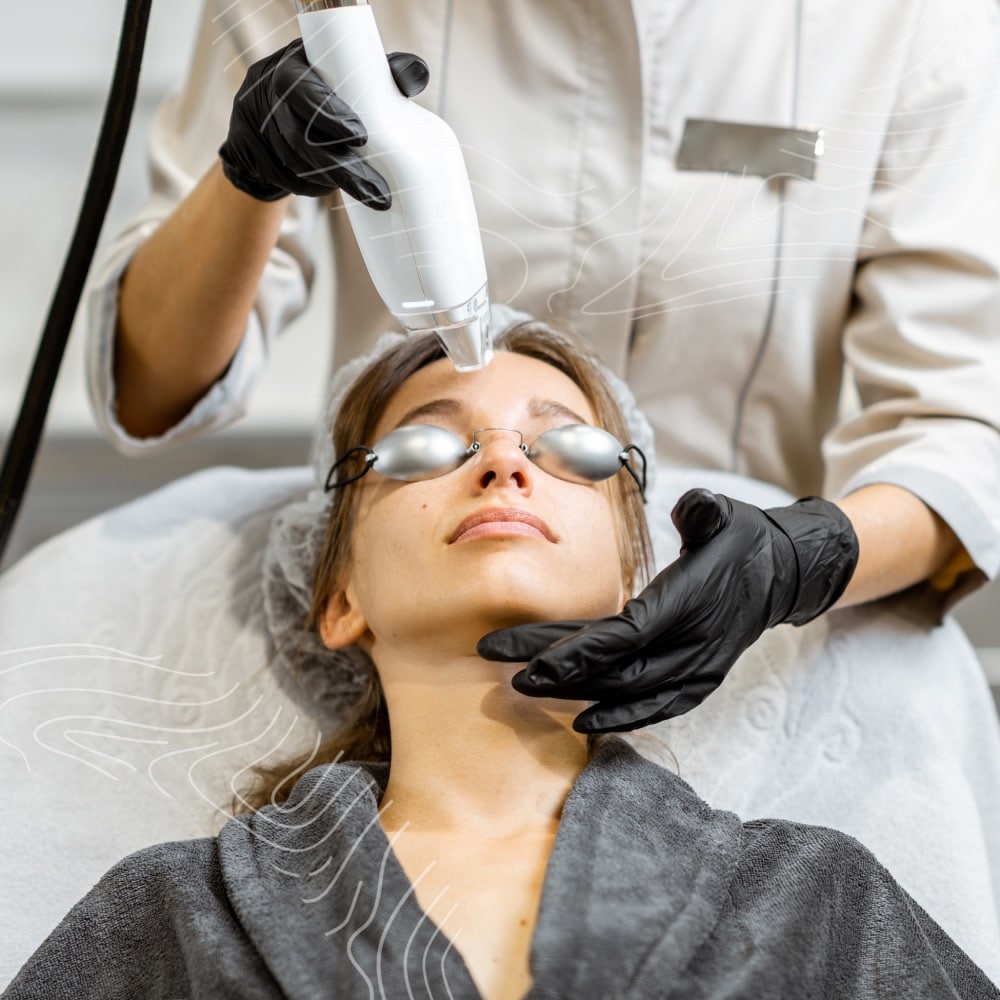 A woman undergoing a skincare treatment with a handheld device while wearing protective glasses, administered by a technician in gloves.