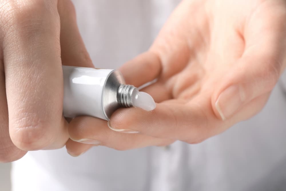 A person applies ointment from a small, white tube onto their fingertip, prepping for skin resurfacing treatment.