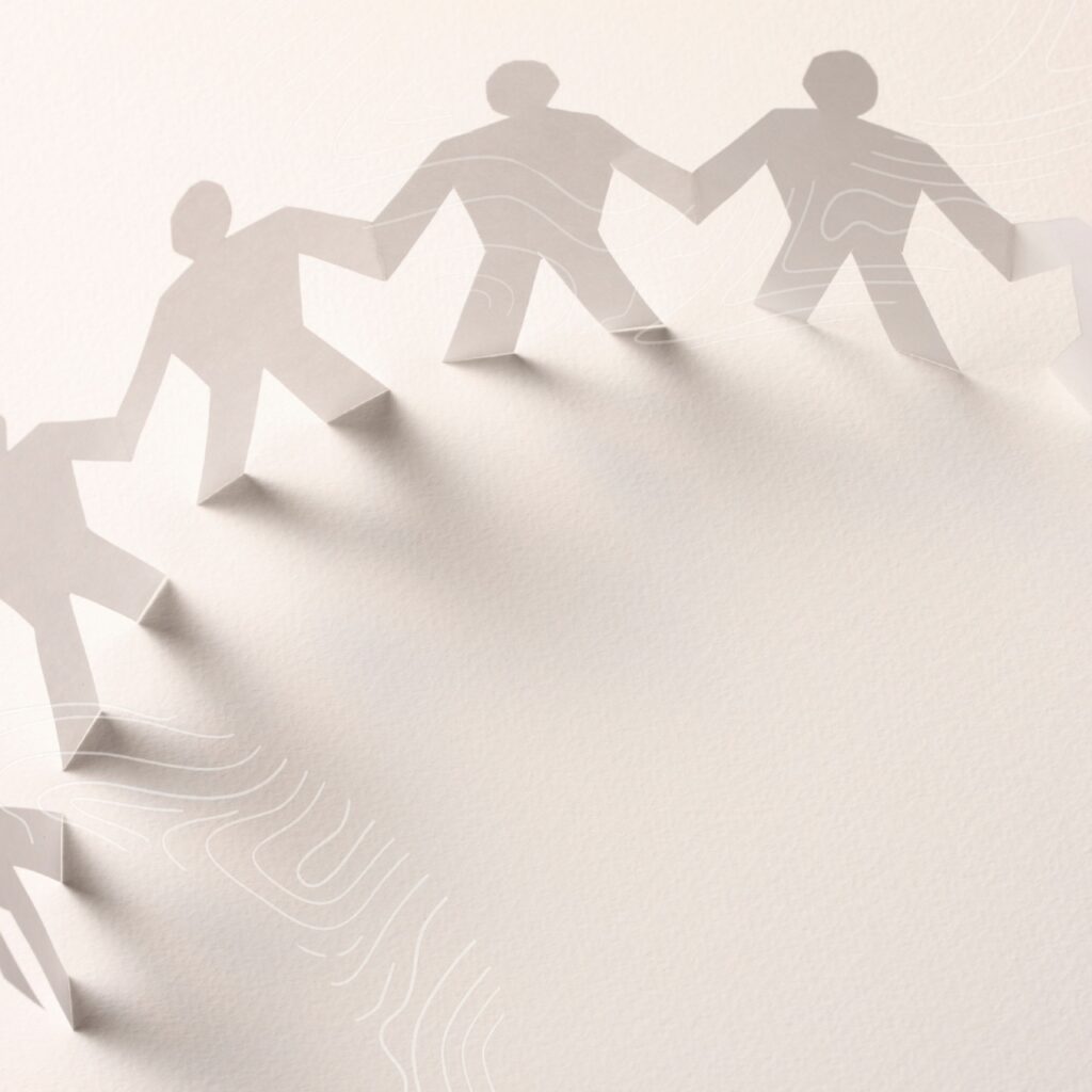 A paper chain of human silhouettes holding hands casts shadows on a light, textured surface, symbolizing the unity and dedication of medical professionals in healthcare.