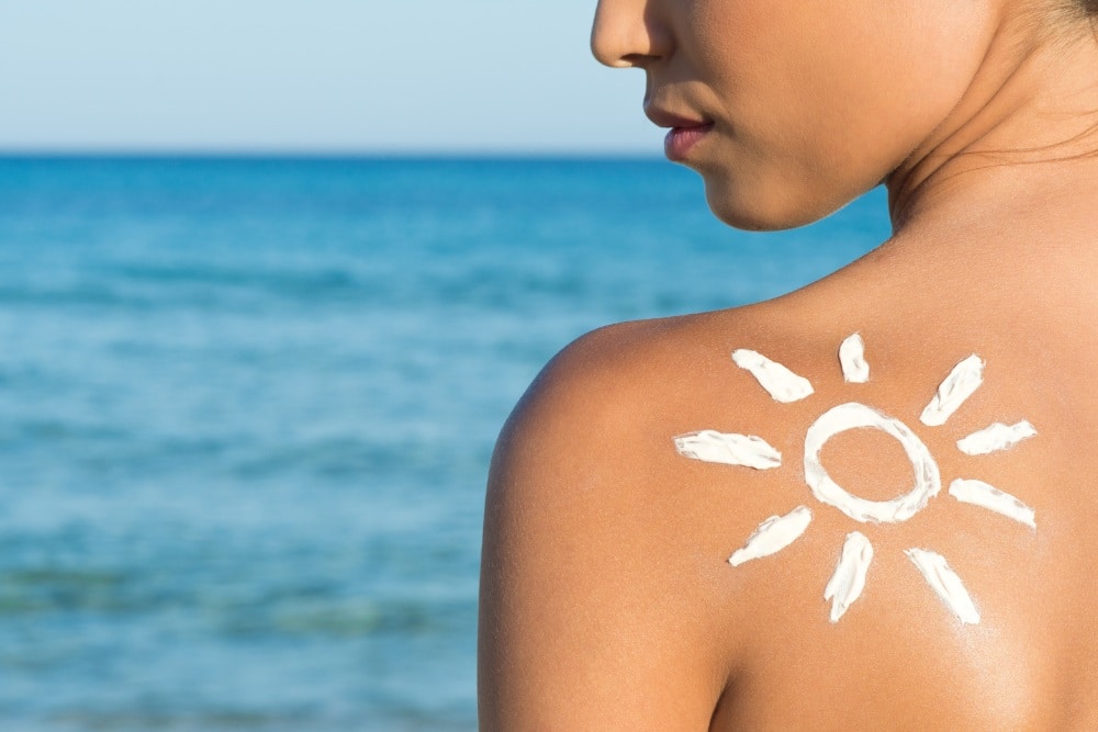 A person with sunscreen in the shape of a sun drawn on their shoulder stands in front of the ocean on a sunny day, exemplifying healthy skin practices that complement non-ablative laser resurfacing treatments.