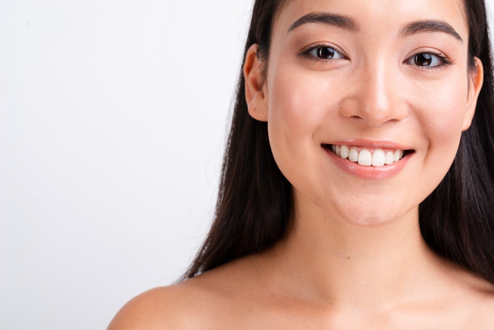 A woman with long dark hair smiles at the camera against a plain white background, radiating confidence as she embraces her journey with scar treatments.