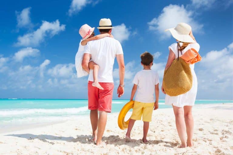 A family of four walks on a sandy beach, with the ocean and sky in the background. Conscious of how genetics have impact on skin cancer risks.