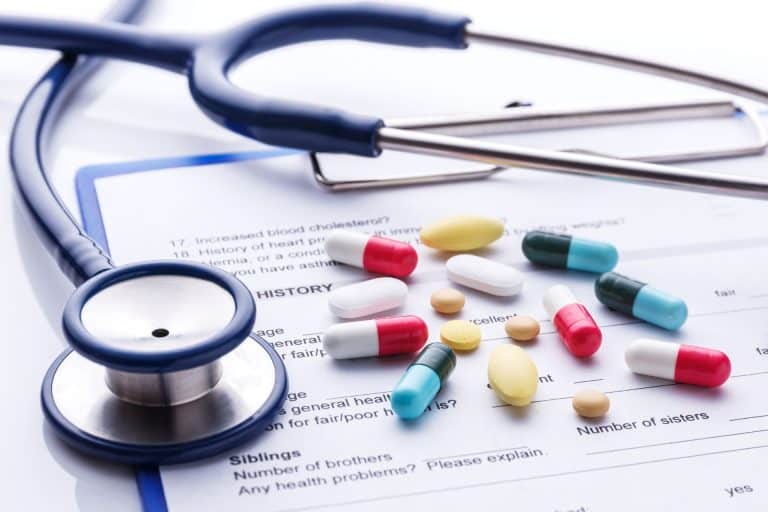 A stethoscope and various pills lie atop a medical history form, highlighting higher chance of skin cancer risks with medication and weakened immune system.