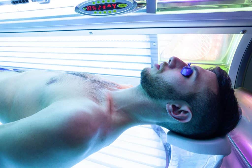 Person lying in a tanning bed with protective eyewear while mindful of the impact and risks of developing melanoma skin cancer.