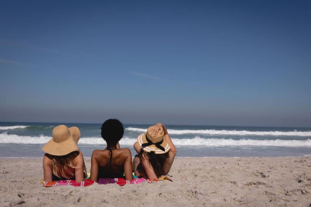 Three people sunbathing at the beach under the sun while aware of how climate and outdoor activities have impact on skin cancer risks.