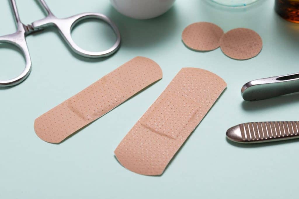 Two adhesive bandages and two round wound dressings rest on a light blue surface, surrounded by medical instruments and supplies—ideal essentials for practical post-surgical wound care.