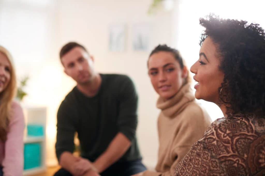 Four people sit in a circle indoors, engaged in conversation about the psychological impact of skin cancer, with one woman speaking while the others listen attentively.