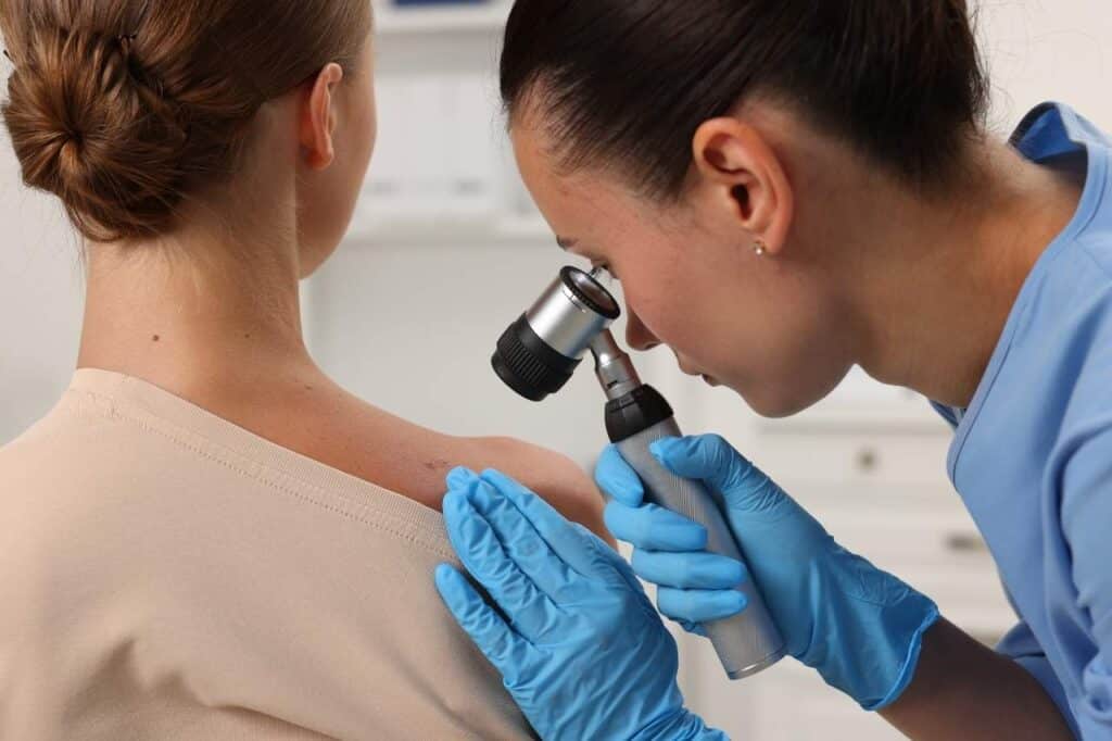 A medical professional examines a mole on a patient's shoulder using a dermatoscope, highlighting the importance of skin cancer prevention.